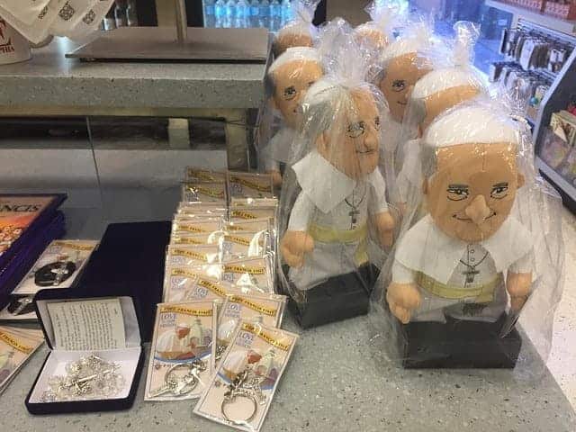 Geschenke mit hässlicher Figur von Bergoglio und Schlüsselanhänger mit Spruch 'Liebe ist unsere Mission'. Mit Bergoglio zur Eine-Welt-Religion.