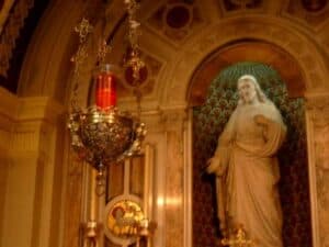 Im Hintergrund eine Herz-Jesu-Statue, im Vordergrund das Ewige Licht